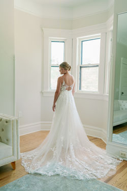 Bride standing at a bay window with her lace train spread behind her