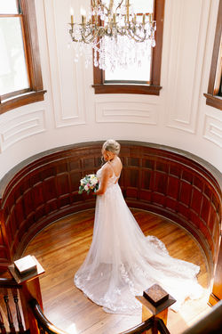 Bride with a long train standing in a curved wooden alcove under a chandelier