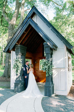 Bride and groom outside a timber wedding chapel framed with greenery