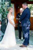Bride and groom exchanging vows beneath a floral arch in a wooden chapel