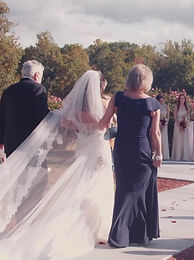 Bride walking down the aisle with her parents, veil trailing behind