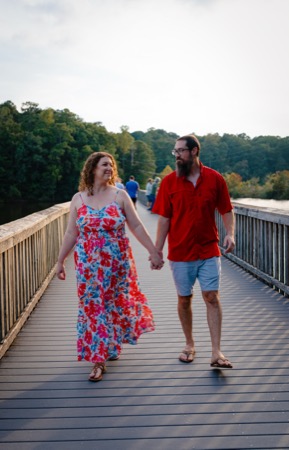 Engagement session photo of a couple walking a lakeside bridge
