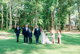 Wedding party of bridesmaids and groomsmen gathered on a wooded lawn